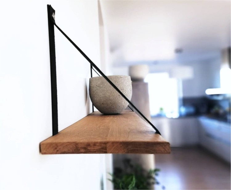 Drewniana półka wisząca z litego dębu na skórzanych paskach, pokazana z boku. Widoczne naturalne słoje i sęki drewna. W tle jasna, gładka ściana w kolorze beżowym podkreślająca minimalistyczny, nowoczesny styl wnętrza.